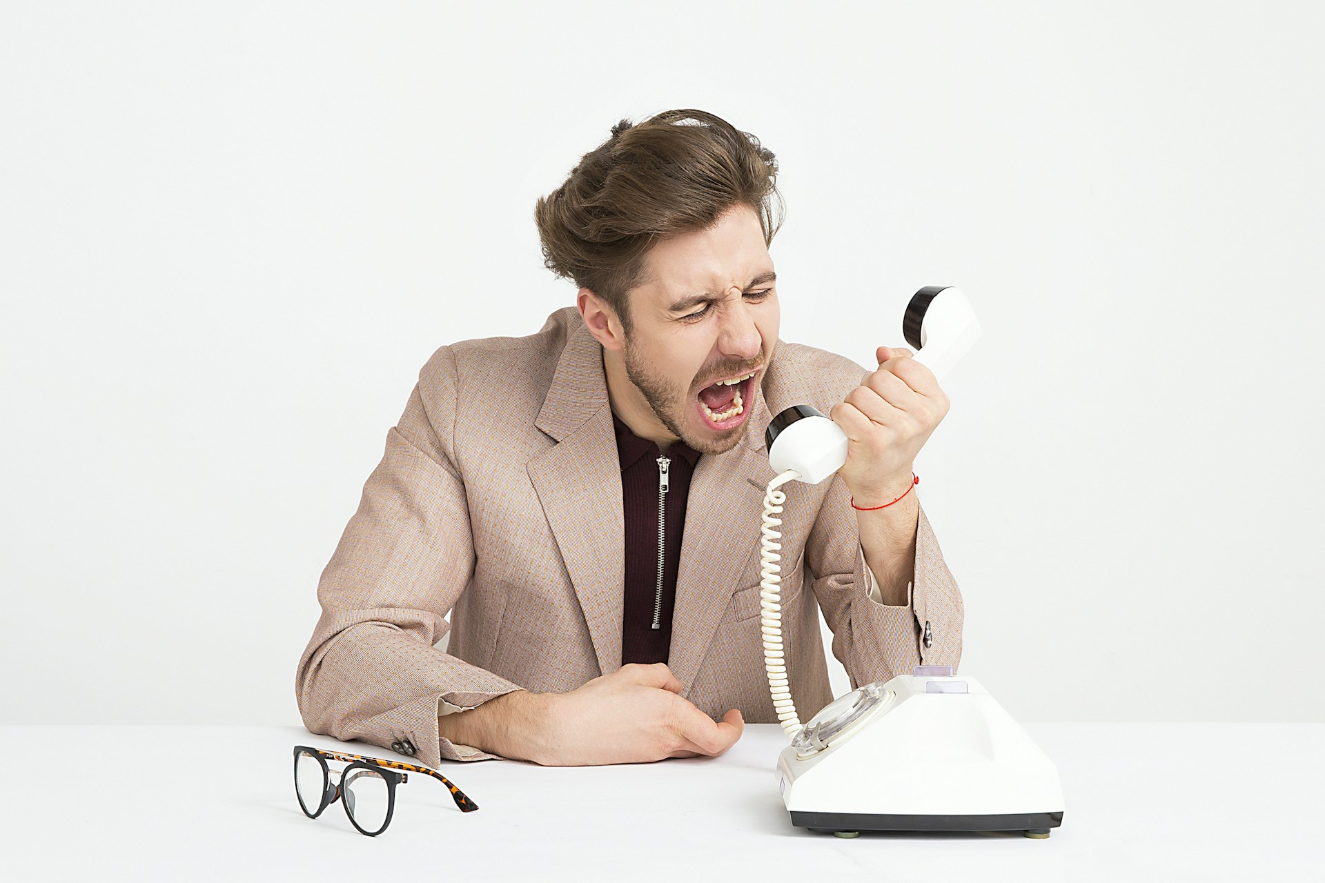 A frustrated man shouting into a telephone at his desk, symbolizing stress in office communication.