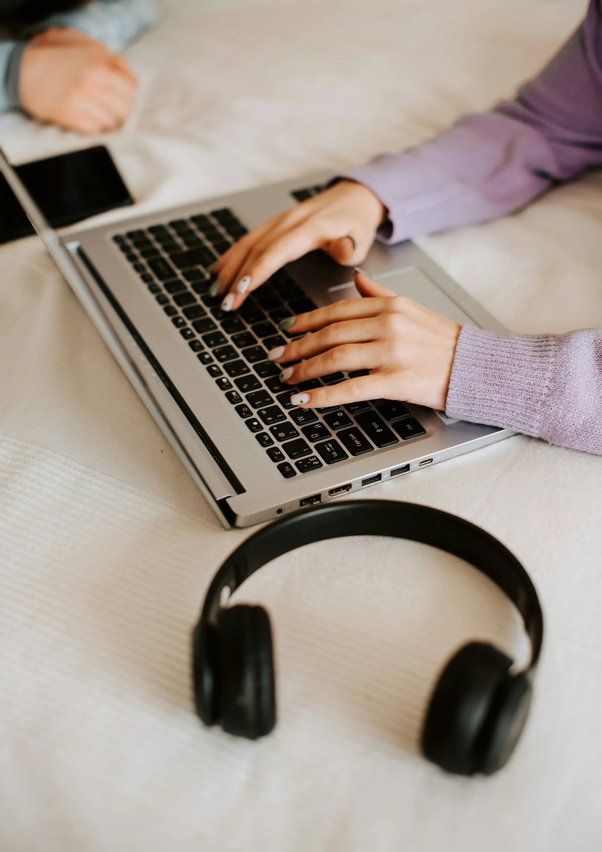 Person working on a laptop with wireless headphones nearby