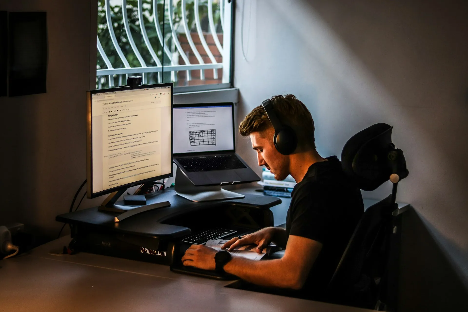 Professional working at a multi-screen workstation with headphones in a home office