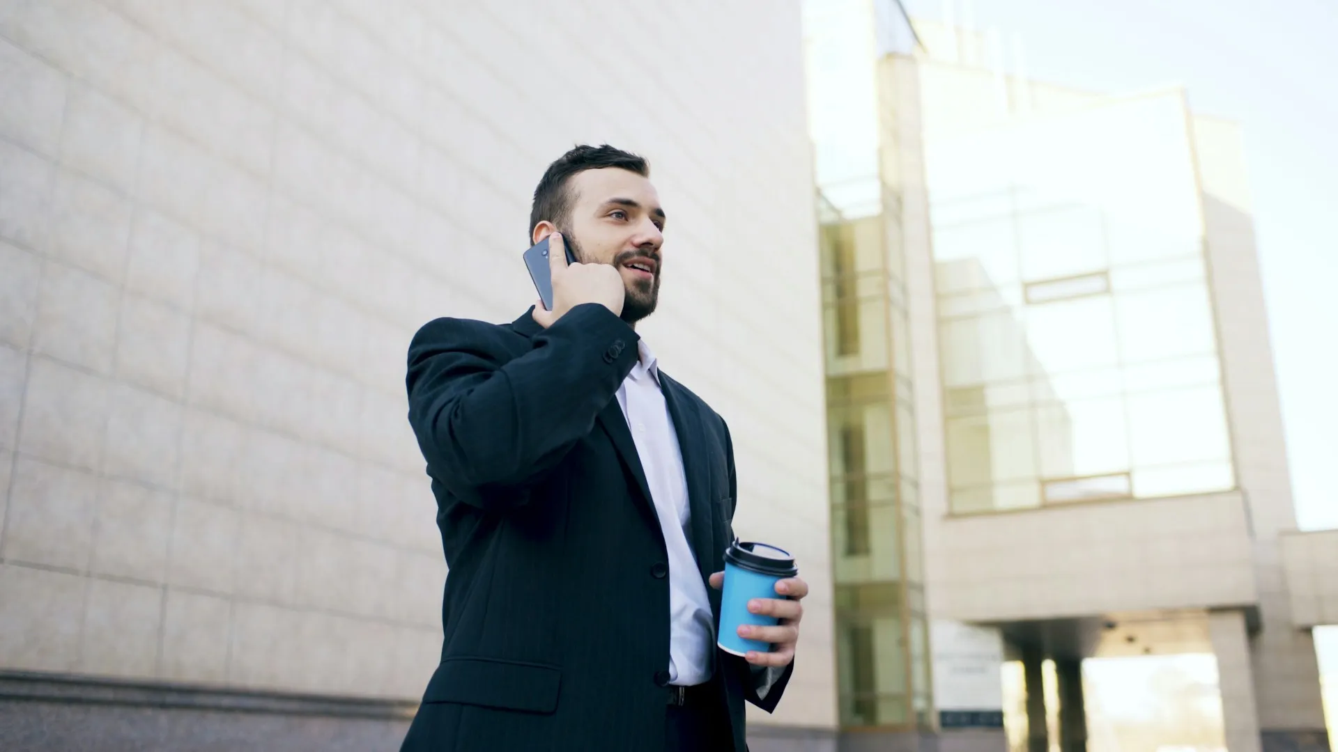 Young businessman in a suit talking on his smartphone near an office building